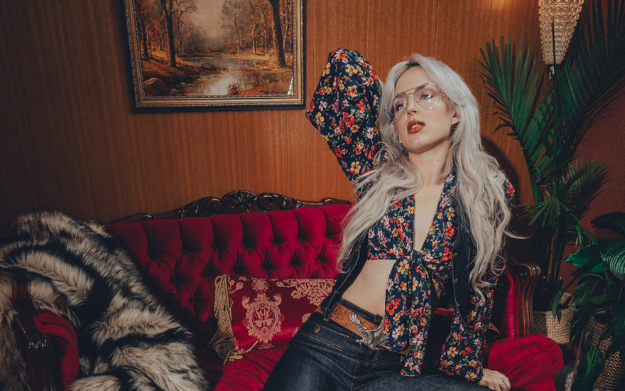 Sexy 1970s style girl wearing a floral retro blouse denim waist coat and bell bottom jeans posed in a vintage 1970s living room