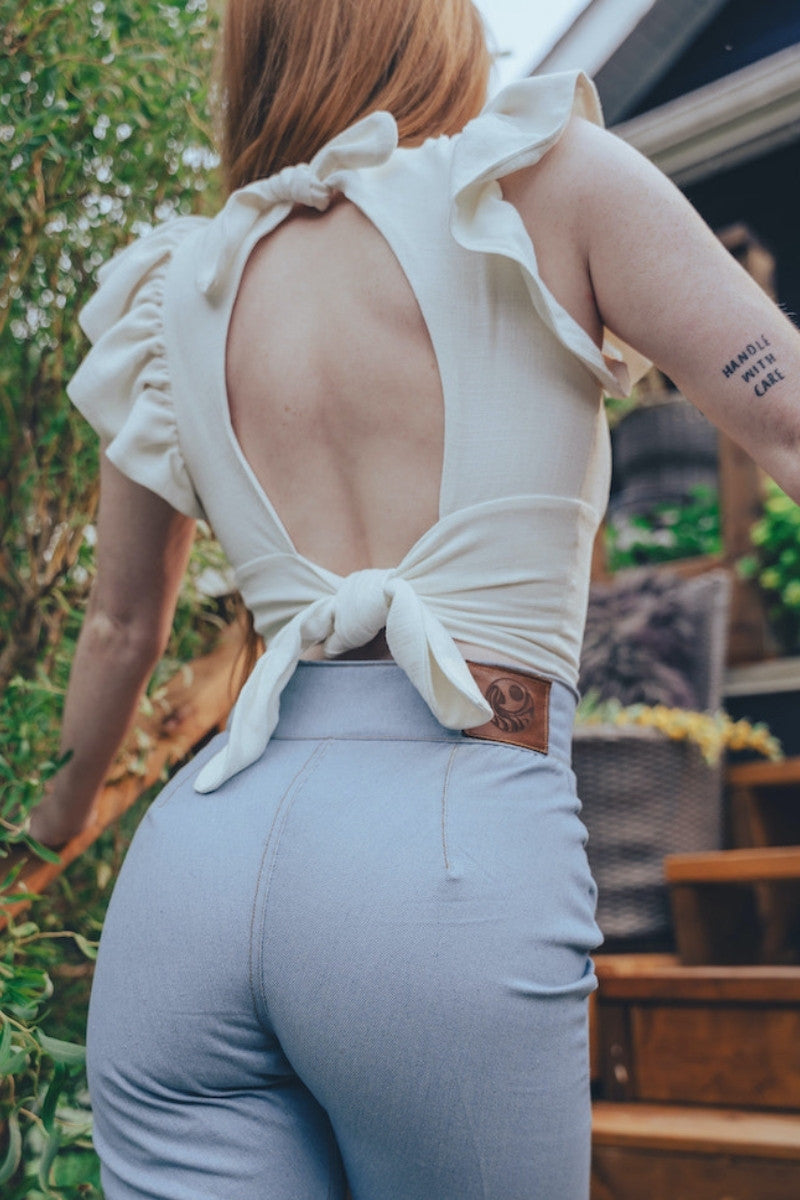 Person wearing a white top with an open back and light blue pants outdoors.