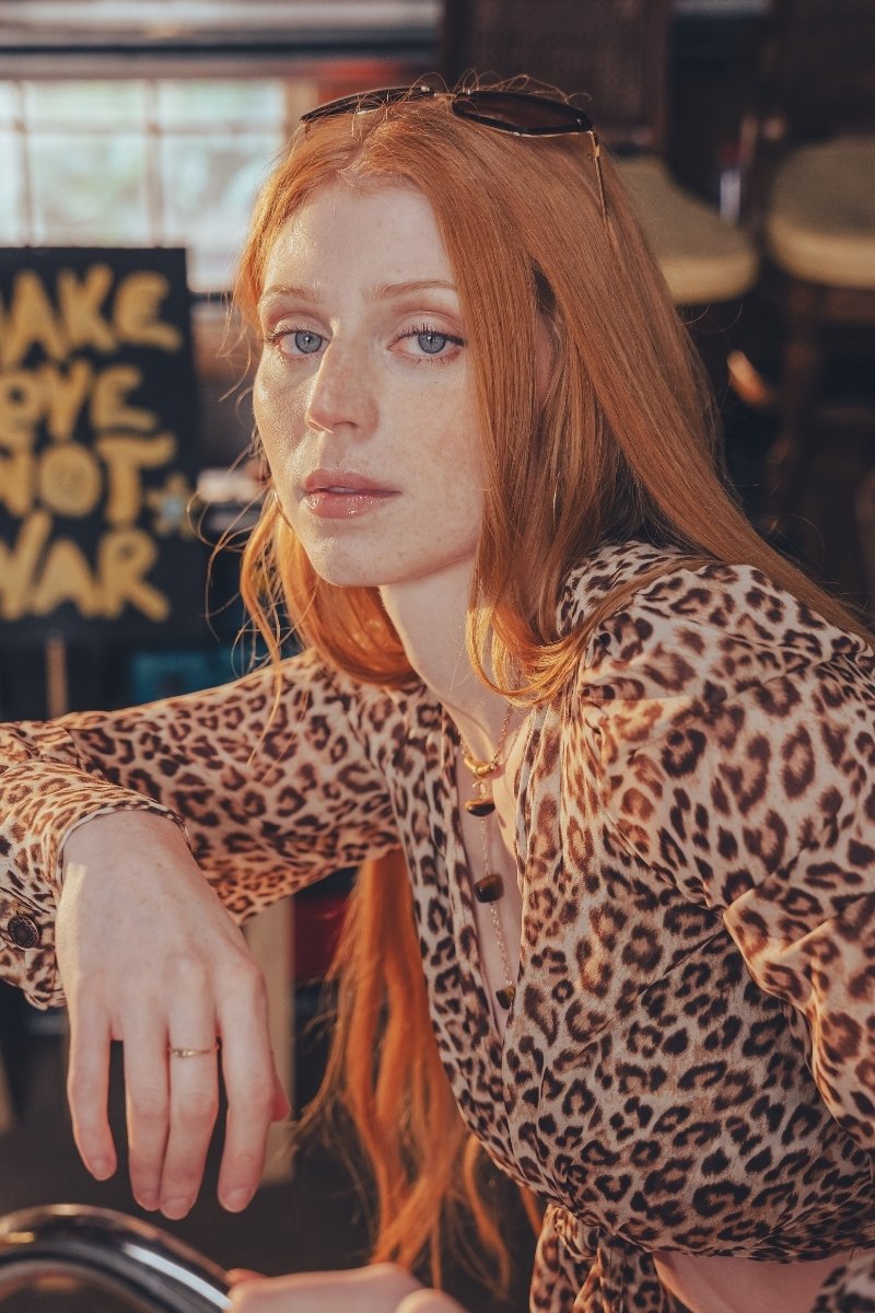Woman with red hair wearing a leopard print top in an indoor setting.