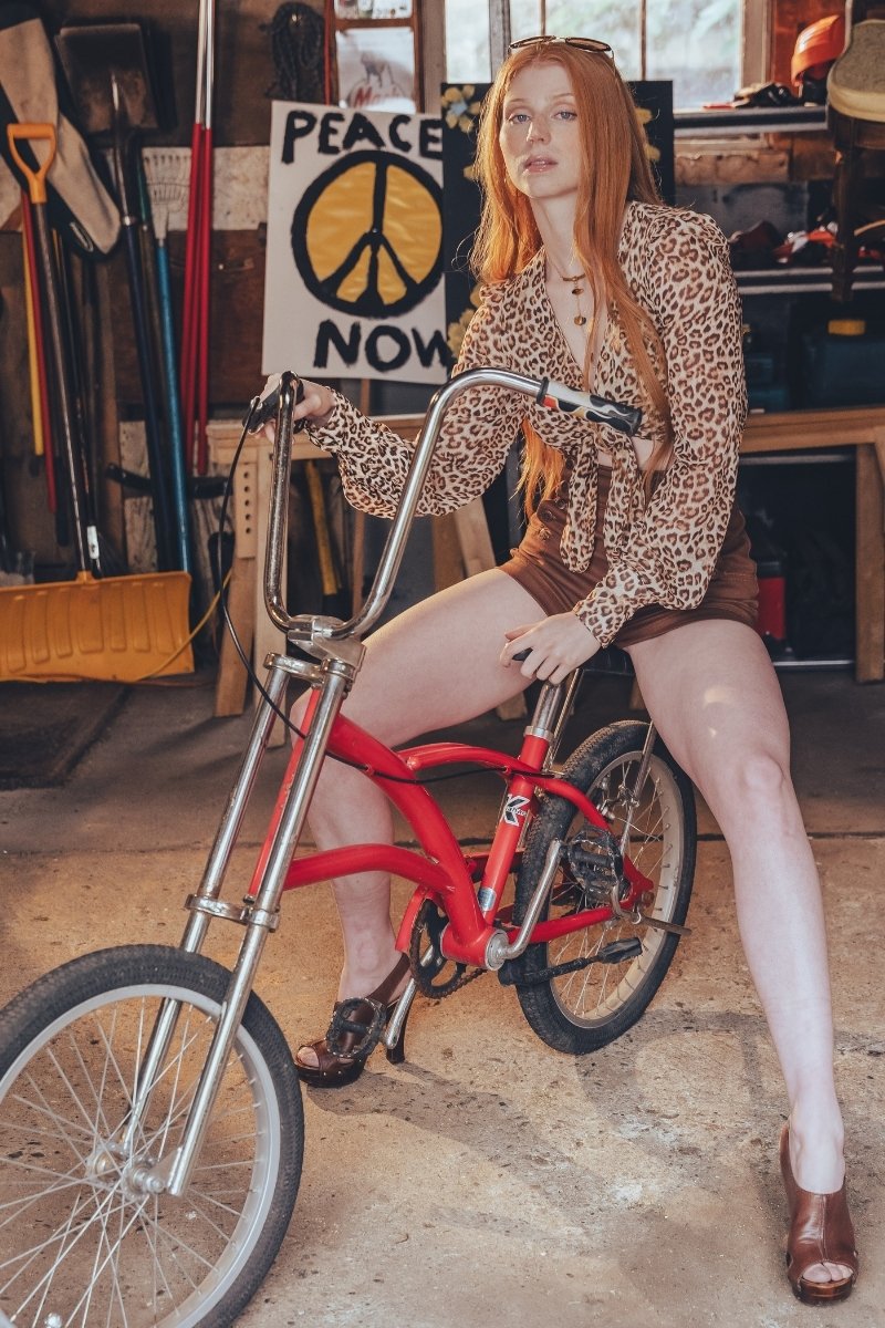 Person in leopard print outfit sitting on a red bicycle in a workshop setting.