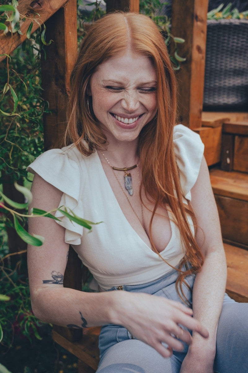 Woman with red hair sitting outdoors, surrounded by greenery