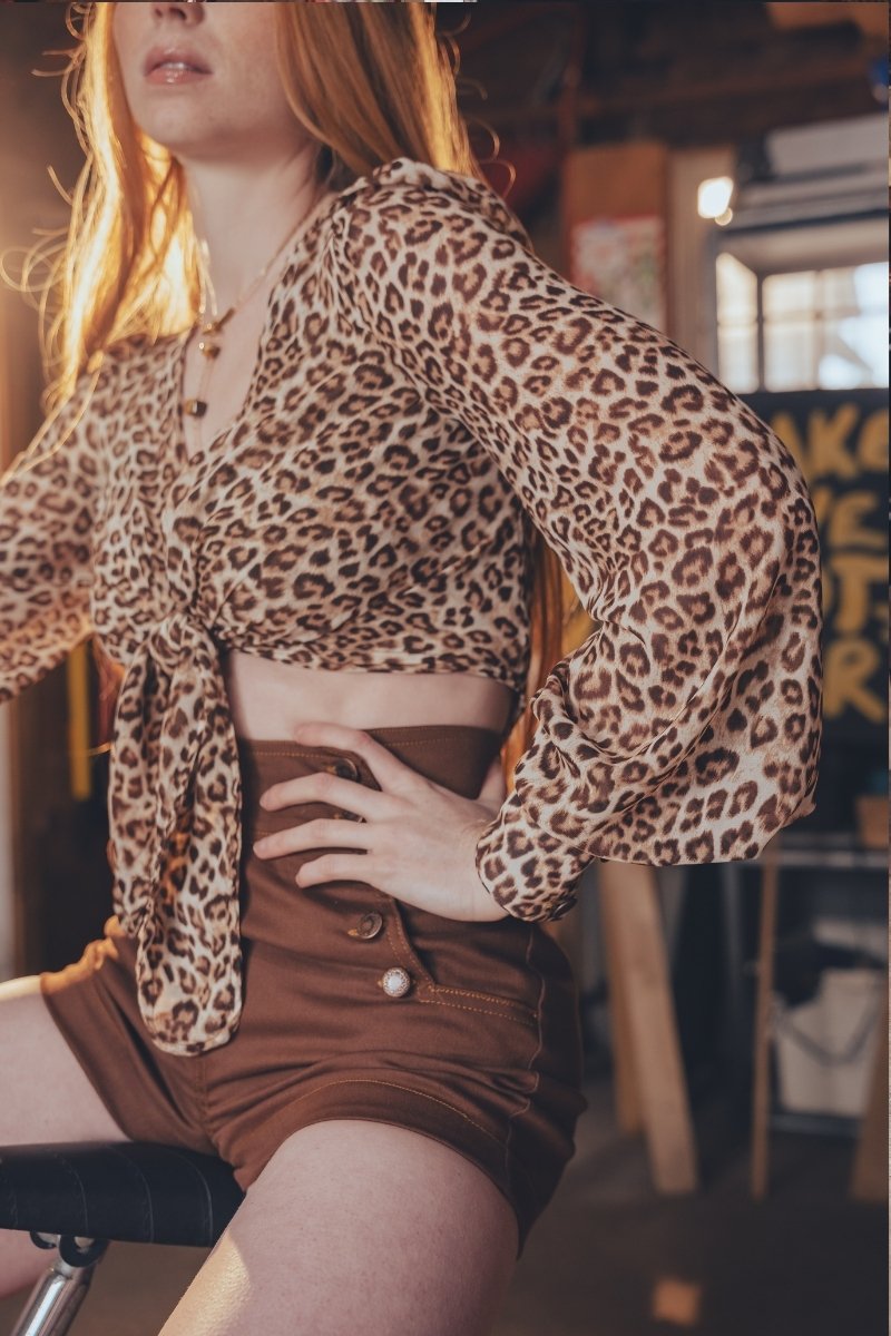 Person wearing a leopard print top and brown shorts in an indoor setting.