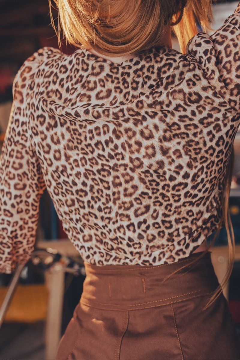 Person wearing a leopard print top and brown pants in an indoor setting