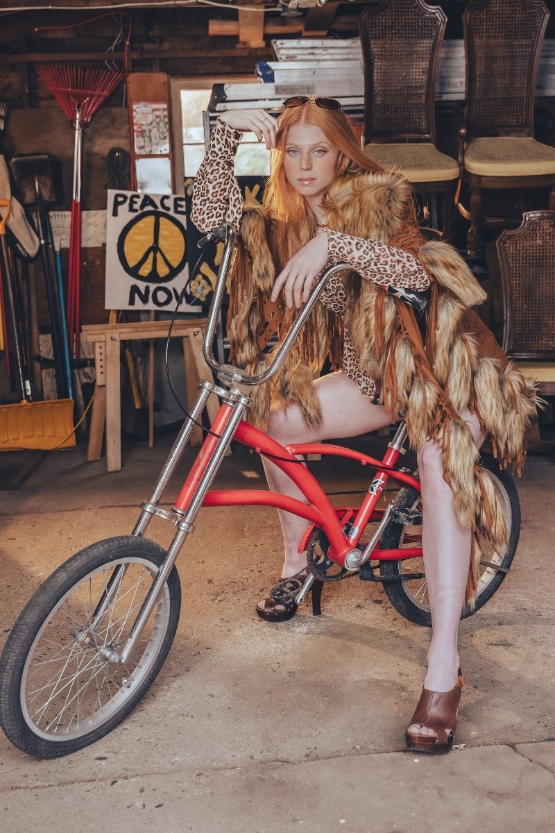 Person sitting on a red bicycle in a cluttered room with chairs and a 'Peace Now' poster.