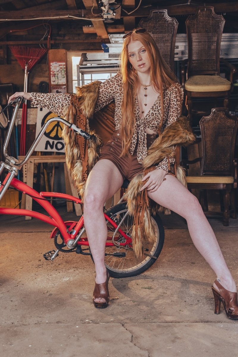 Woman in a vintage setting with a red bicycle and wicker chairs.