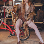 Woman in a vintage setting with a red bicycle and wicker chairs.