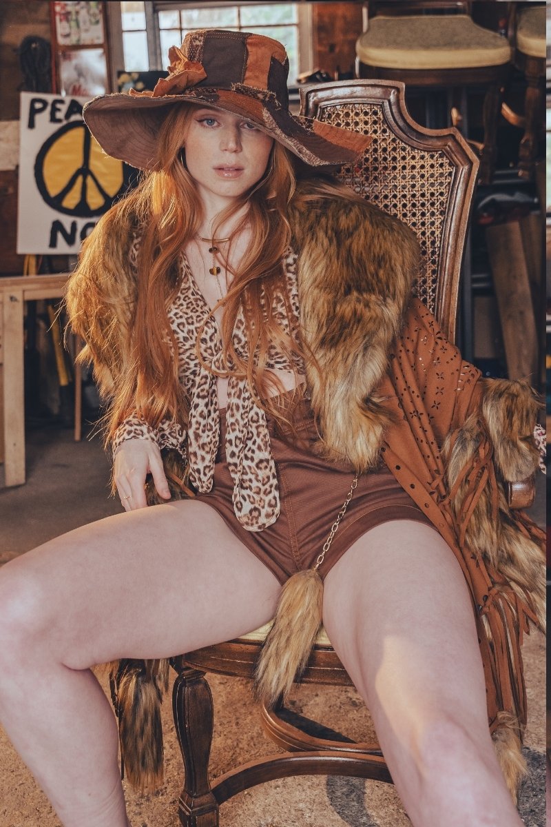 Woman in a vintage-style outfit with a fur stole sitting on a chair in a rustic setting.