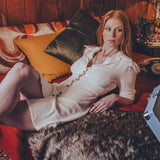 Woman in a white dress lying on a red couch with wooden walls and a lamp in the background