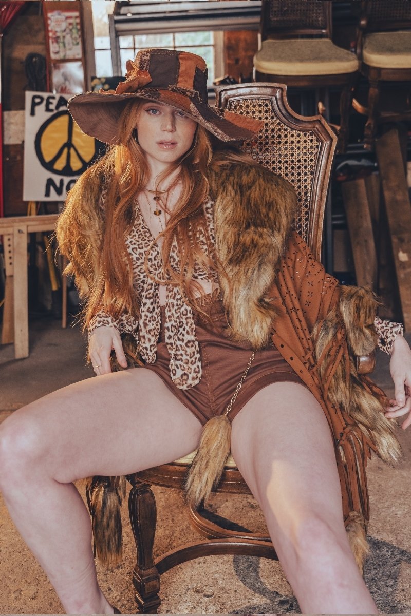 Woman in a vintage-style outfit with a large hat and fur trim sitting on a chair.