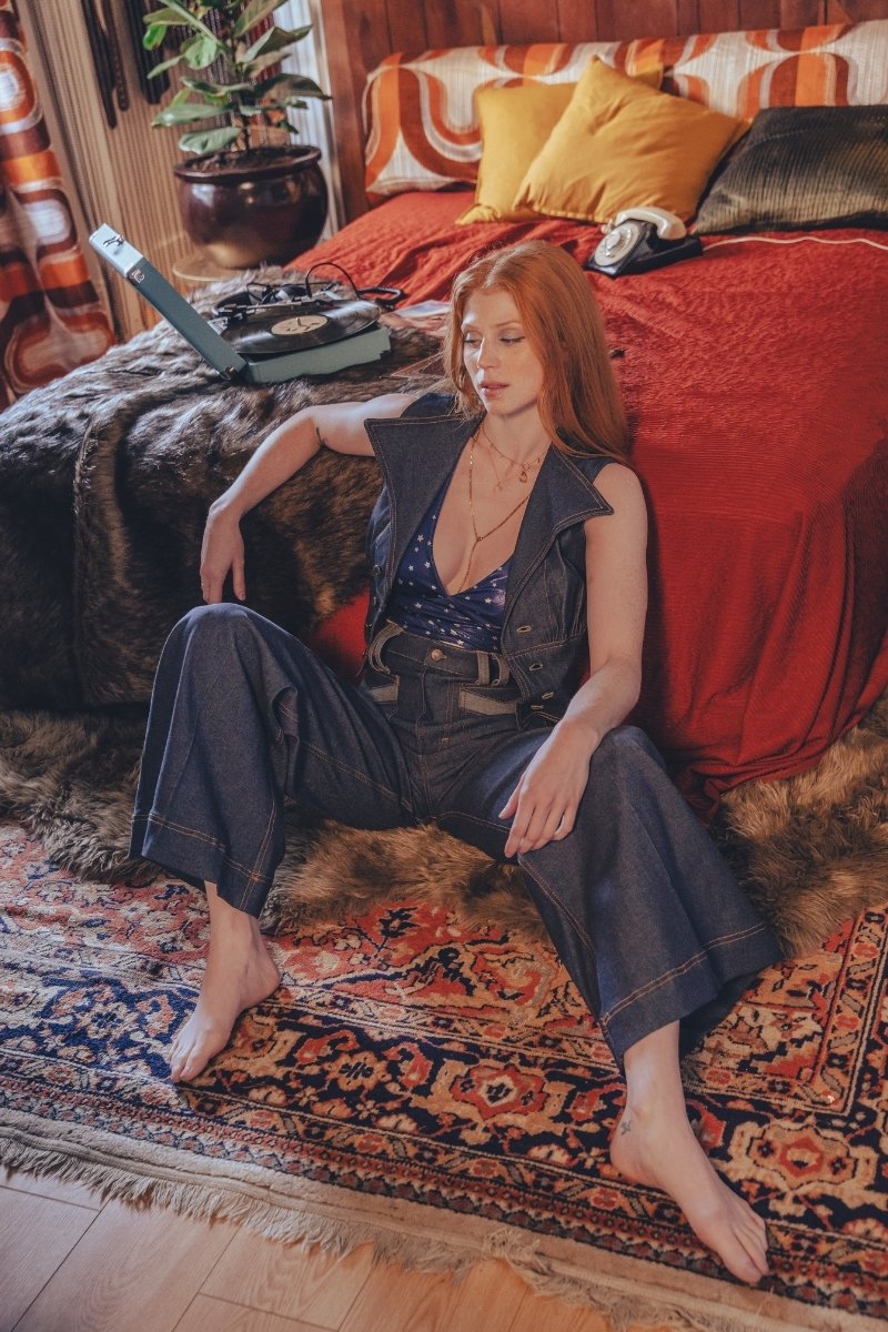 Woman sitting on a patterned rug in a bedroom with a red bedspread and colorful pillows.