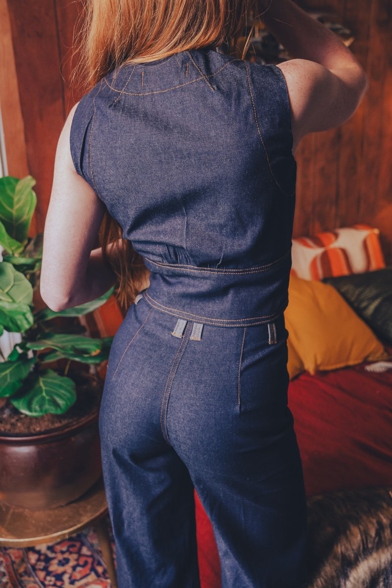 Person wearing a blue denim jumpsuit in a room with a plant and colorful cushions.