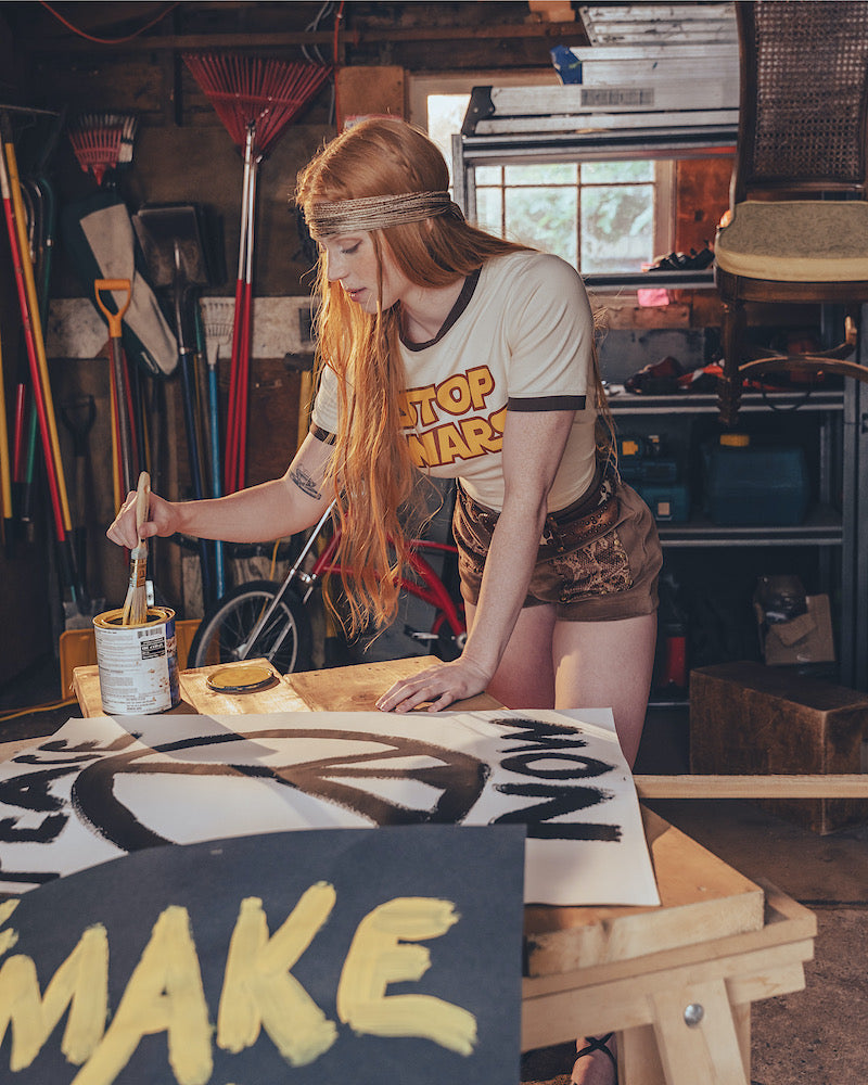 Person painting a peace sign wearing a 'STOP WARS' tee shirt on it in a workshop.