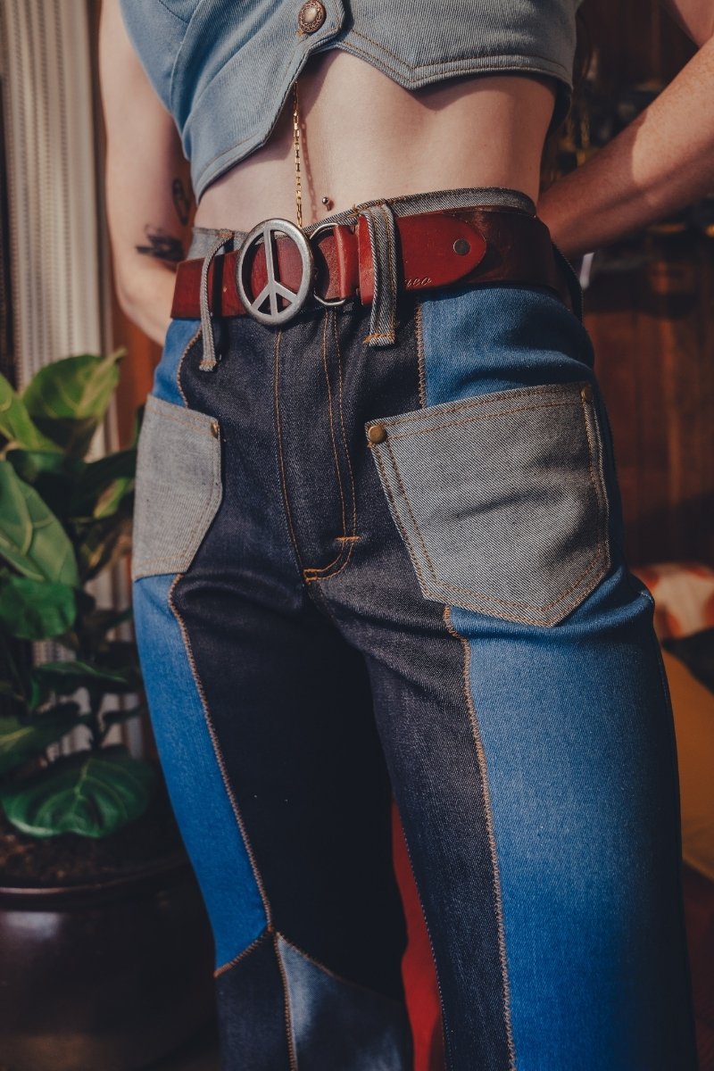 Person wearing patchwork jeans with a peace sign belt buckle.