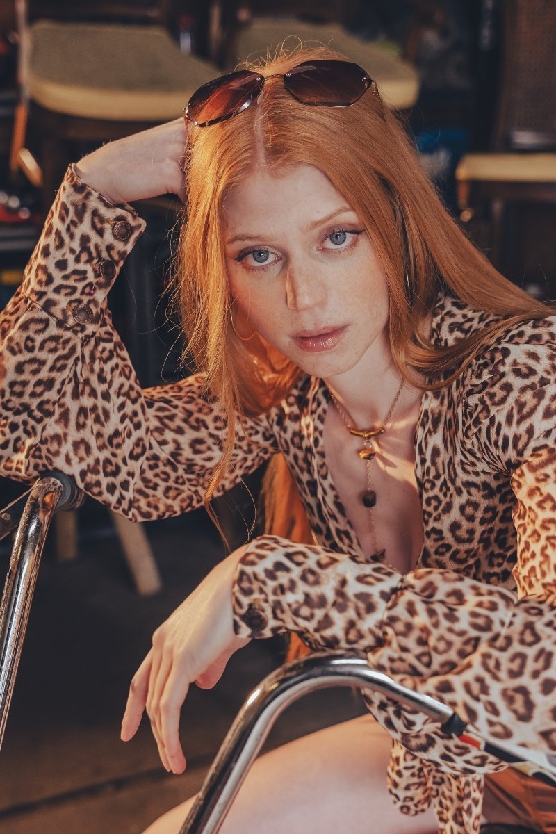 Beautiful redheaded woman sits on a bike wearing a long sleeve leopard print blouse