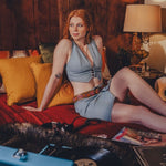 Woman in a blue outfit sitting on a couch in a cozy room with a lamp and pillows.