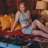 Woman in a blue outfit sitting on a couch in a cozy room with a lamp and pillows.