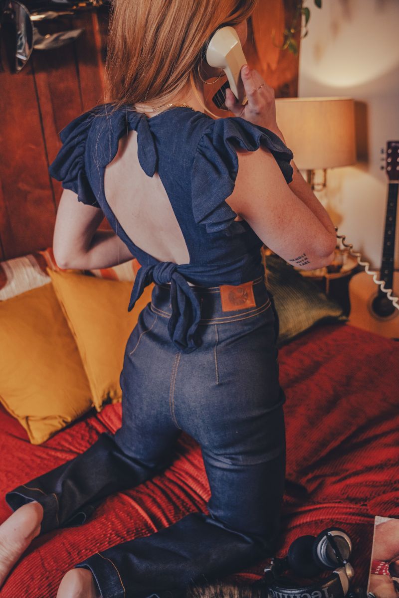 Person wearing a blue denim outfit with a visible brand logo, standing on a red couch.