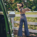 A person posing by a fence wearing high waisted bell bottoms and a sleeveless top.