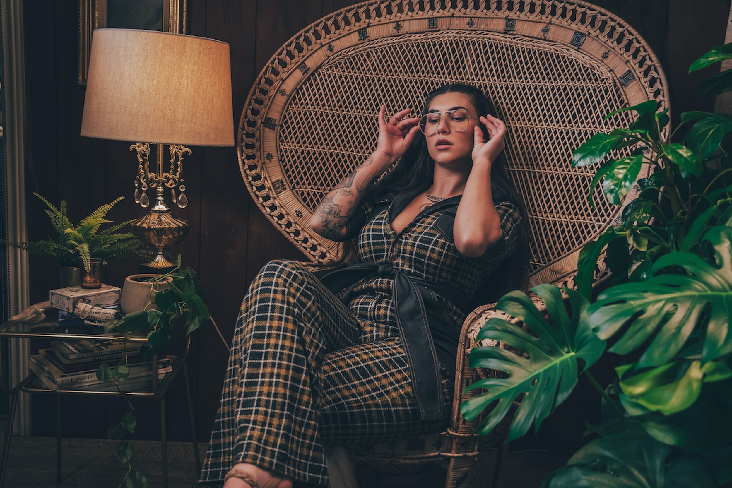 Curvy woman in a plaid knit diva jumpsuit sitting confidently in a vintage 1970s peacock chair exuding retro glam and feminine power