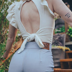 Person wearing a white top with an open back and light blue pants outdoors.