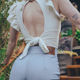 Person wearing a white top with an open back and light blue pants outdoors.