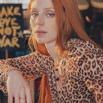 Woman with red hair wearing a leopard print top in an indoor setting.