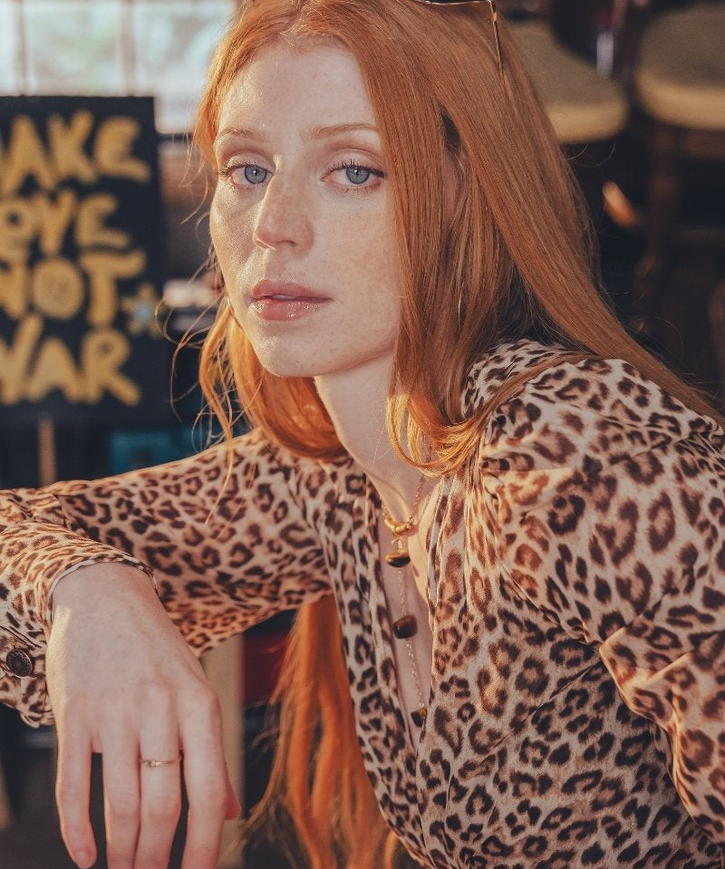 Woman with red hair wearing a leopard print top in an indoor setting.