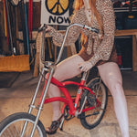 Person in leopard print outfit sitting on a red bicycle in a workshop setting.