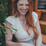 Woman with red hair sitting outdoors, surrounded by greenery