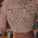 Person wearing a leopard print top and brown pants in an indoor setting