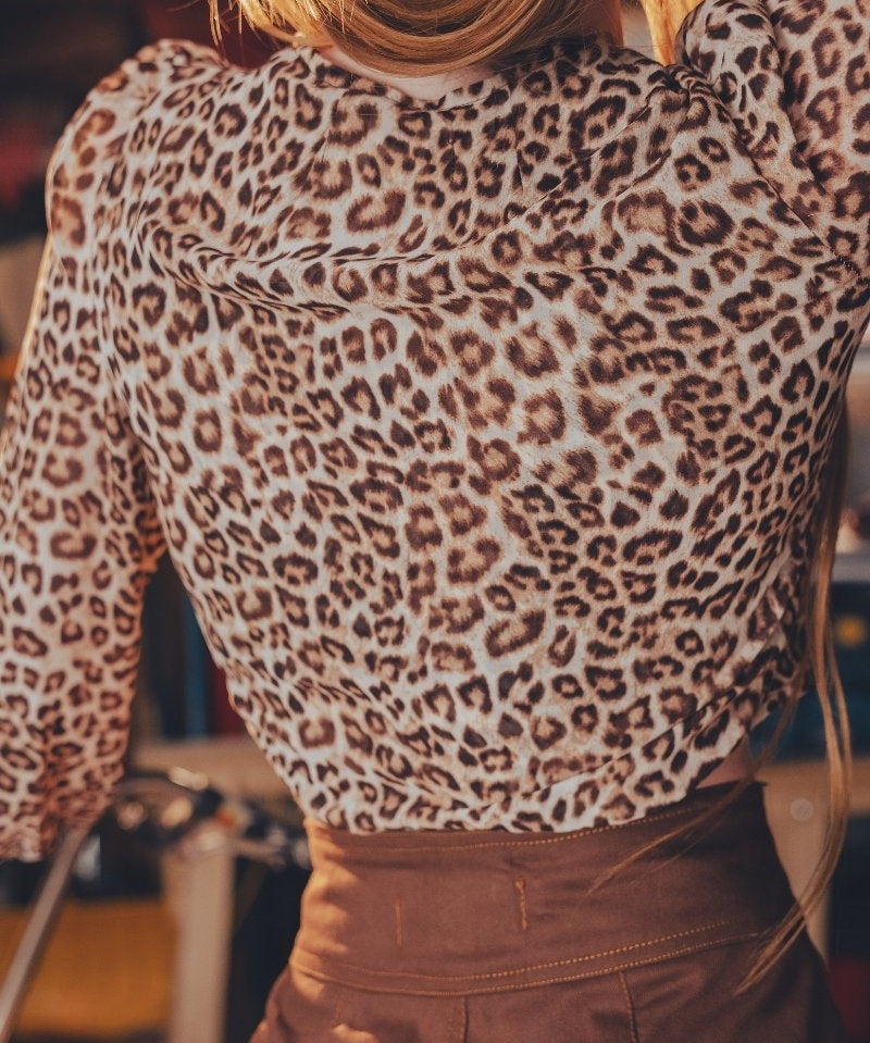 Person wearing a leopard print top and brown pants in an indoor setting