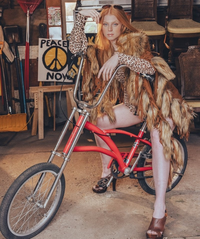 Person sitting on a red bicycle in a cluttered room with chairs and a 'Peace Now' poster.