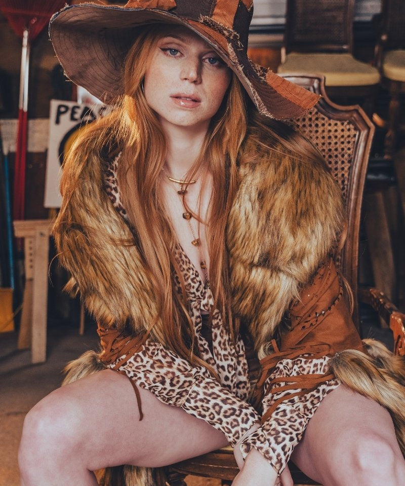 Person wearing a fur-trimmed outfit with a hat, sitting in a rustic setting.