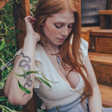 Woman with red hair sitting outdoors near plants and wooden furniture