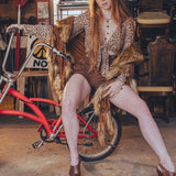 Woman in a vintage setting with a red bicycle and wicker chairs.