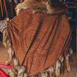 Person wearing a brown poncho with fur trim and intricate patterns, standing next to a red bicycle.