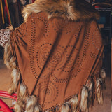 Person wearing a brown poncho with fur trim and intricate patterns, standing next to a red bicycle.