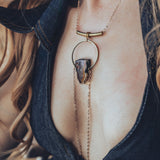 A person wearing a gold-plated chain necklace with a teardrop-shaped pendant that drapes over the chest.