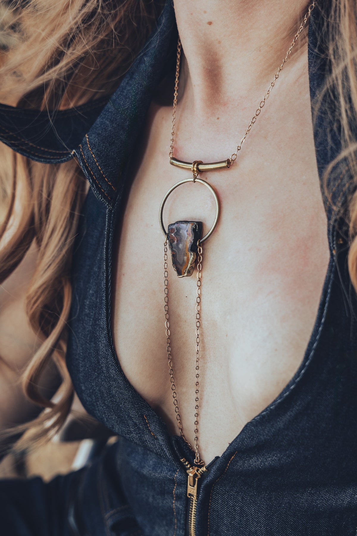 A person wearing a gold-plated chain necklace with a teardrop-shaped pendant that drapes over the chest.