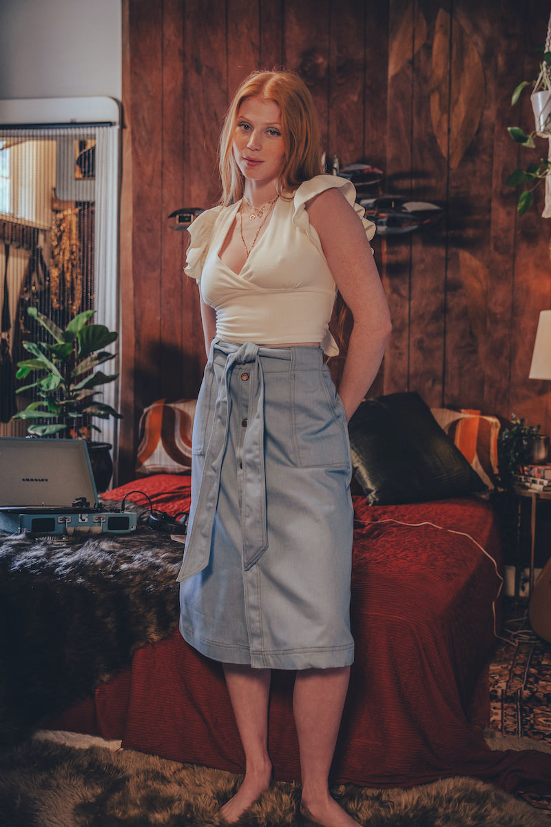 Woman standing in a bedroom with wooden walls and a bed in the background