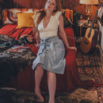 Woman sitting on a bed in a cozy room with wooden walls and a guitar.
