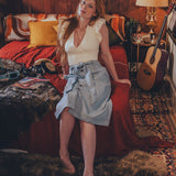 Woman sitting on a bed in a cozy room with wooden walls and a guitar.