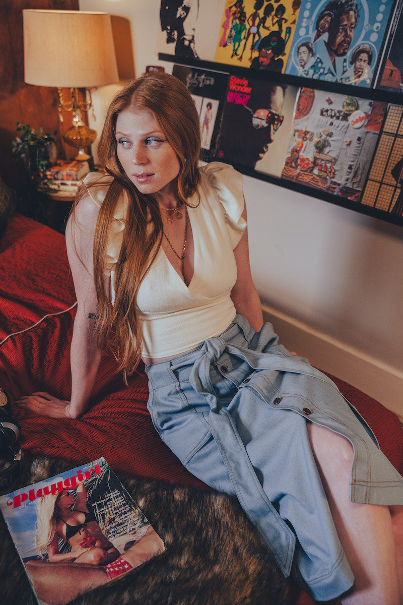 Woman sitting on a couch with a magazine and a dog, surrounded by posters on the wall.