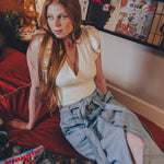 Woman sitting on a couch with a magazine and a dog, surrounded by posters on the wall.
