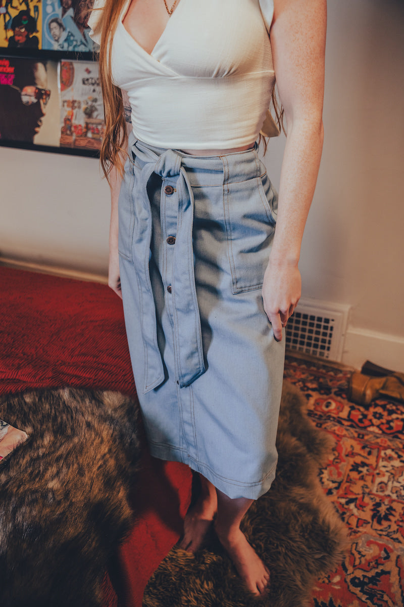 Person wearing a white top and blue denim skirt in a room with a red rug and colorful wall art.