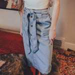 Person wearing a white top and blue denim skirt in a room with a red rug and colorful wall art.