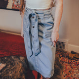 Person wearing a white top and blue denim skirt in a room with a red rug and colorful wall art.