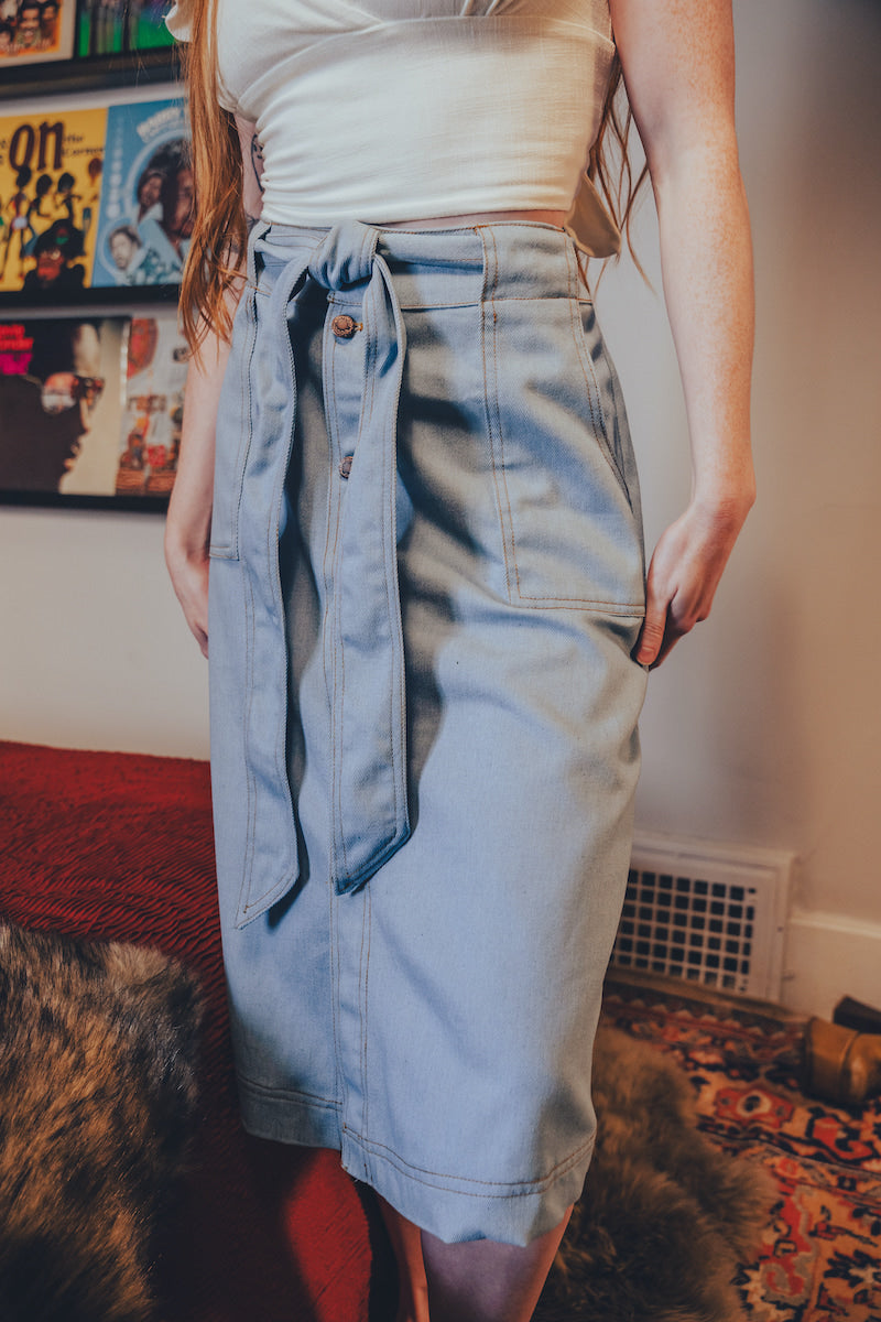 Person wearing a light blue denim skirt with a white top in an indoor setting.