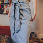 Person wearing a light blue denim skirt with a white top in an indoor setting.