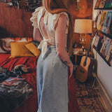 Woman in a light blue dress standing in a cozy bedroom with a guitar and books.